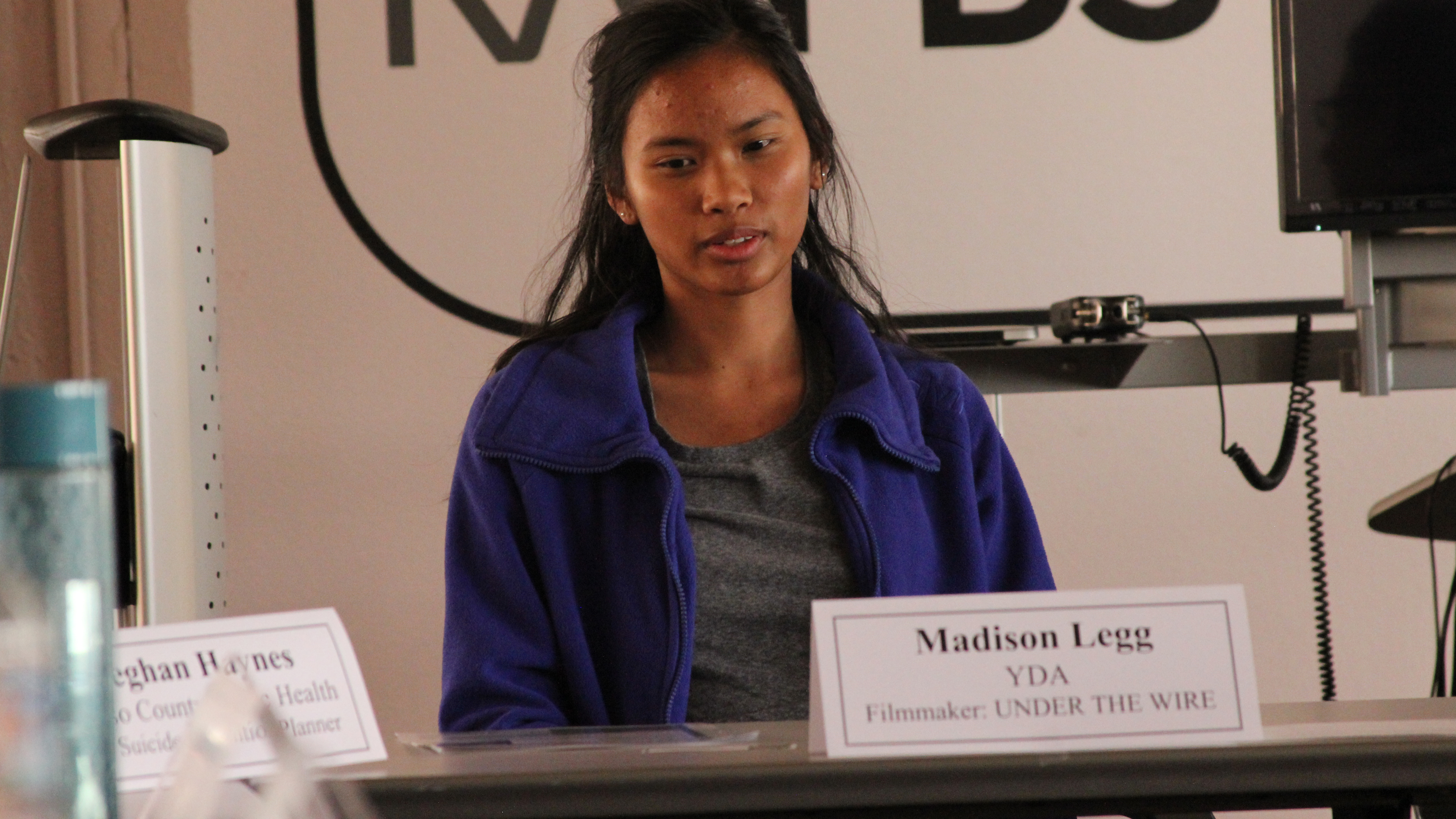 Film still from UNDER THE WIRE, Dir. by Madison Legg, Photo of Madison Legg presenting her film at a suicide prevention conference. Courtesy of Tom Shepard and Youth Documentary Academy